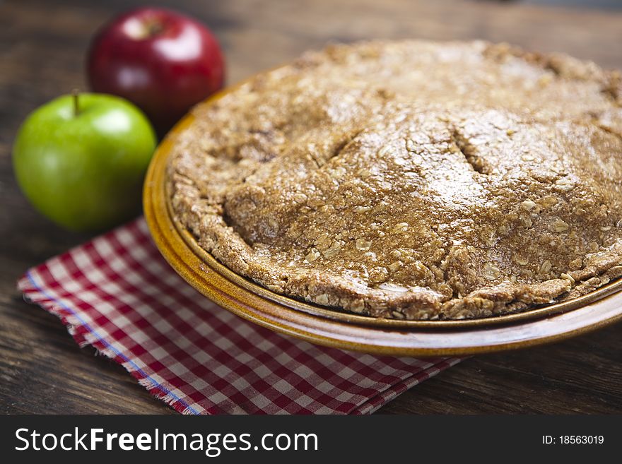 This photograph contains an image of a home baked apple pie in a picnic setting with a red and green apple