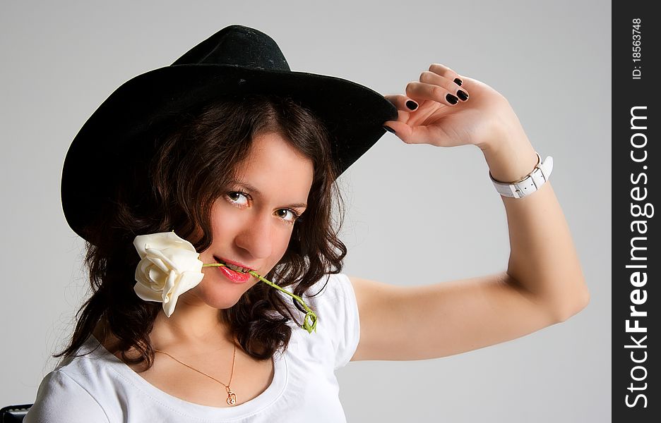 Young woman in black hat with white rose in her mouth posing in studio. Young woman in black hat with white rose in her mouth posing in studio