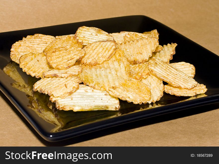 Crinkle potato crisps on a square plate against a brown background. Crinkle potato crisps on a square plate against a brown background