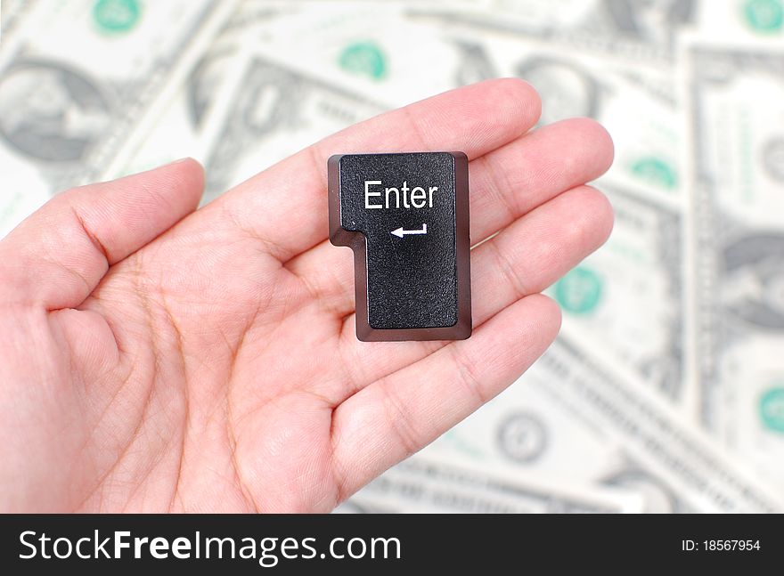 Hand holding an enter key with dollars in the background. Hand holding an enter key with dollars in the background