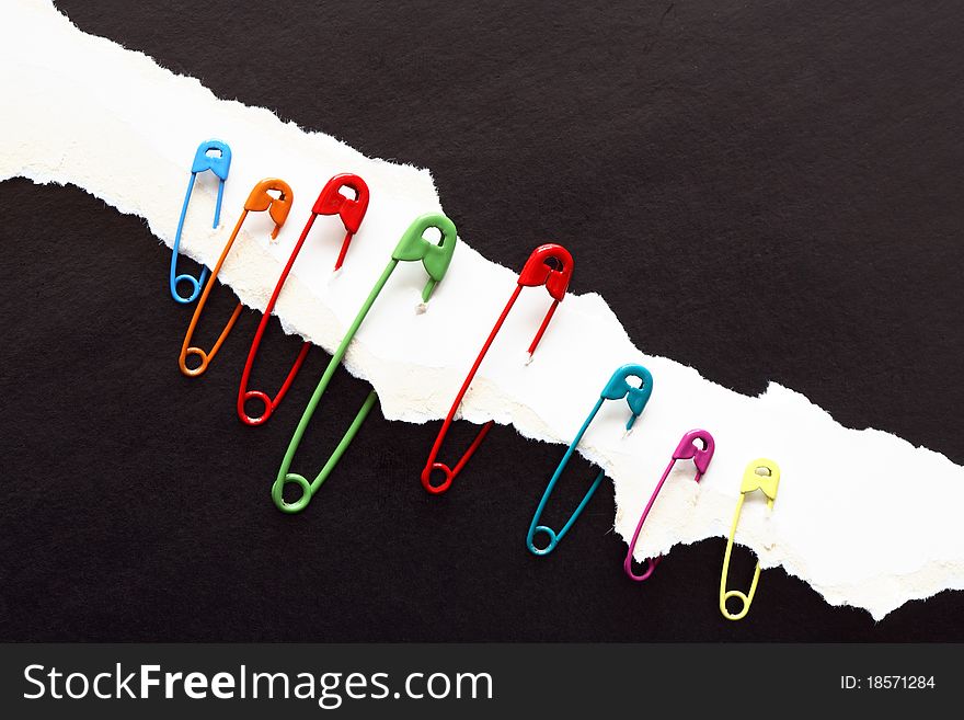 Set of color safety pins constrained to disrupt white paper on black background