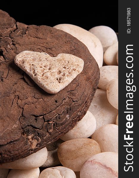 Stone heart on top of a piece of smooth bark, some white pebbles are seen below. Stone heart on top of a piece of smooth bark, some white pebbles are seen below.