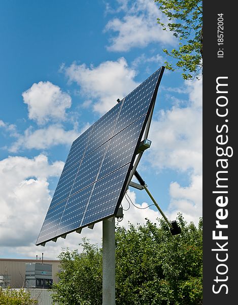 A photovoltaic solar panel array with a blue sky and green leaves in the background. A photovoltaic solar panel array with a blue sky and green leaves in the background.