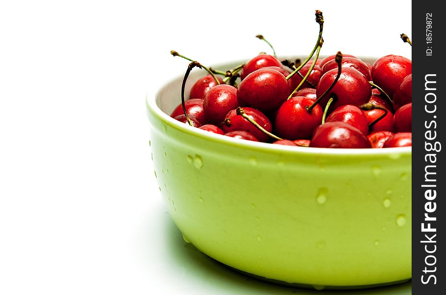 Red cherries in a green bowl with drops of water on ilomu background