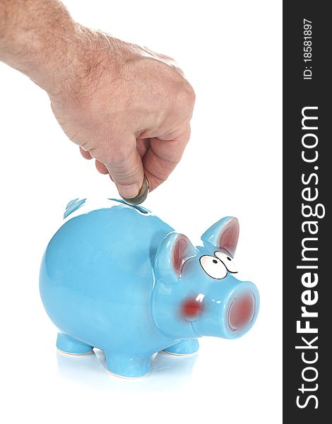 A front studio isolation shot on a white background of a coin being dropped into a blue ceramic piggy bank. A front studio isolation shot on a white background of a coin being dropped into a blue ceramic piggy bank.