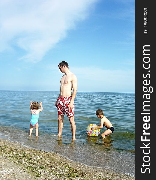 A man plays with a ball at sea with children. A man plays with a ball at sea with children