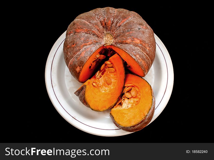 Ripe fresh raw pumpkin on plate isolated over black background. Ripe fresh raw pumpkin on plate isolated over black background