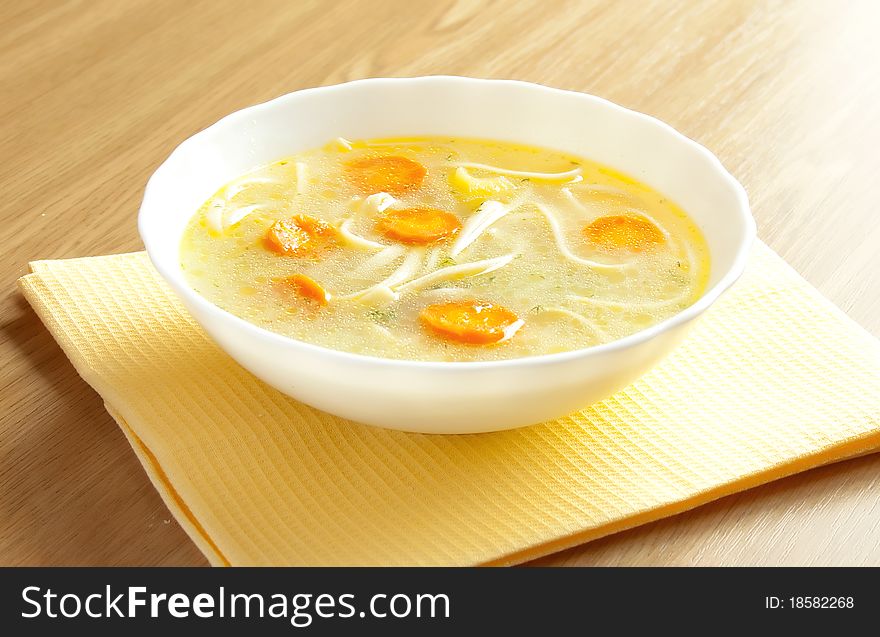 Soup with noodles in a white plate on the yellow cloth