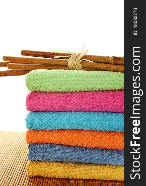 Lots of colorful bath towels stacked on each other. Side by side on a wooden surface lie bamboo sticks. Isolated