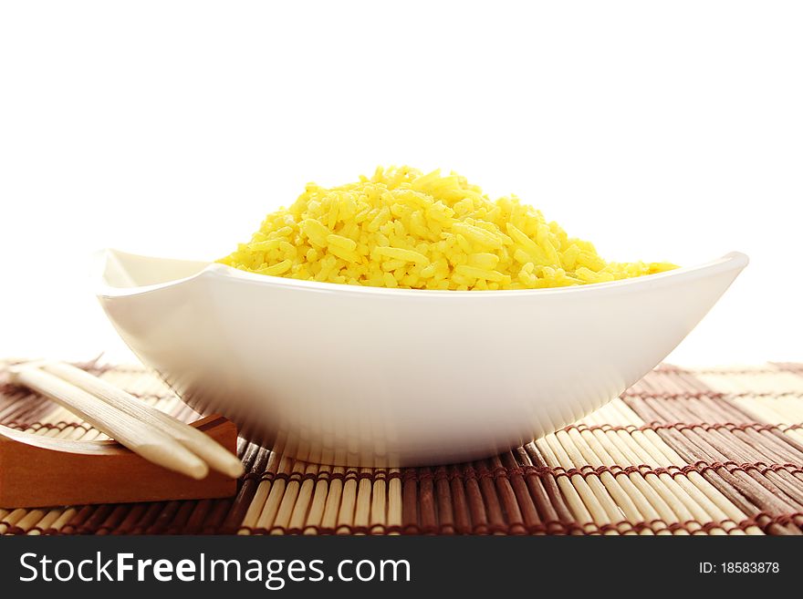 Boiled yellow rice and a white plate beside lie wooden sticks. Plate stands on a wooden mat. Isolated on a white background. Boiled yellow rice and a white plate beside lie wooden sticks. Plate stands on a wooden mat. Isolated on a white background