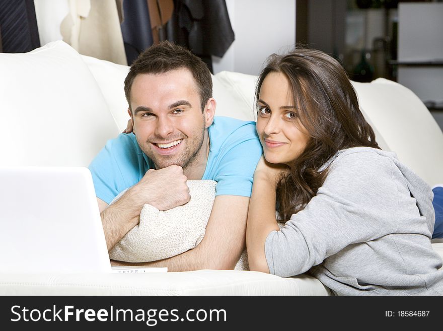 Happy young couple with laptop lying on the white sofa