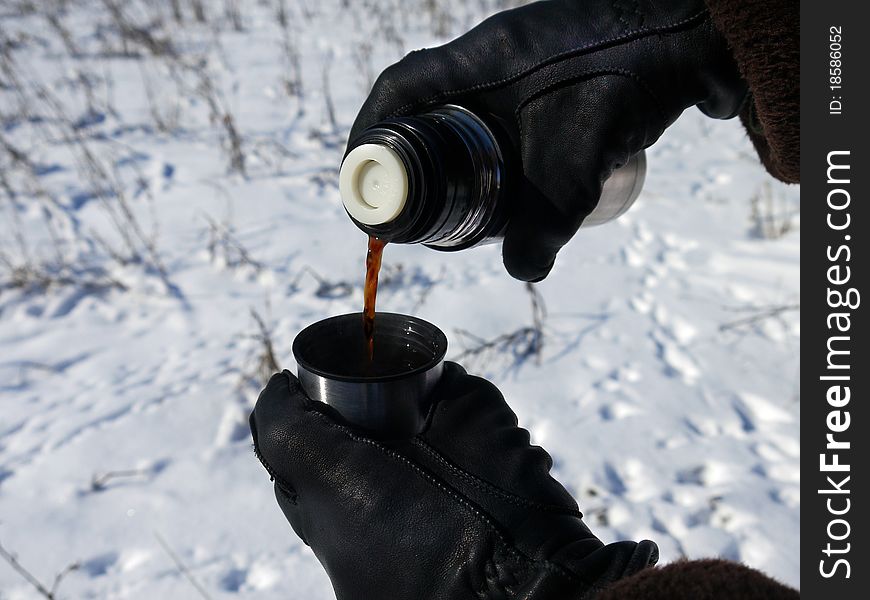 Coffee is poured from a thermos on a background of snow, gloved hands. Coffee is poured from a thermos on a background of snow, gloved hands
