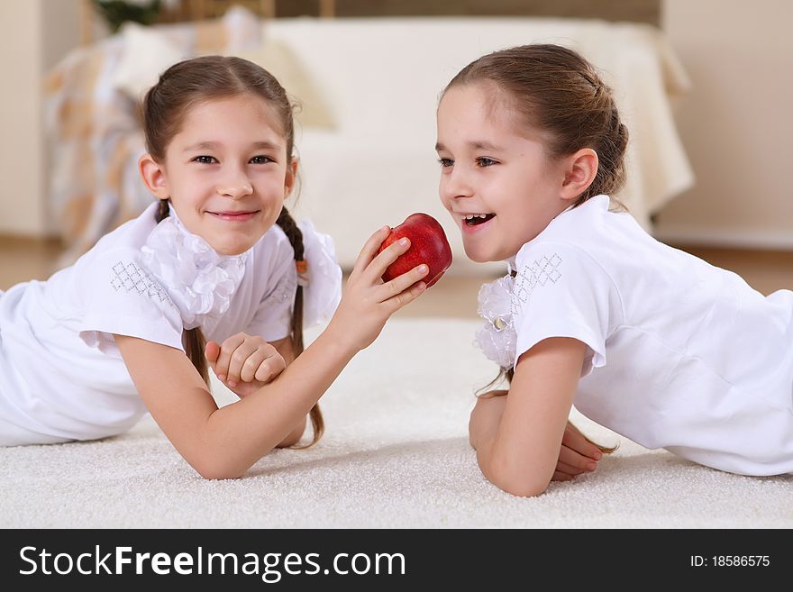 Two twin sisters at home with a red apple. Two twin sisters at home with a red apple