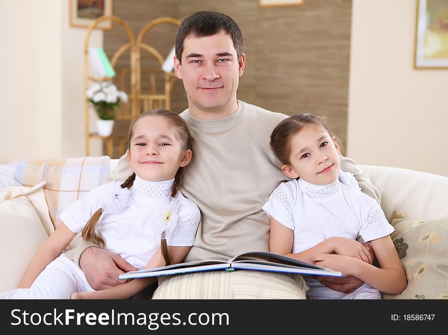 A father with her daughters at home in the living room reading a book. A father with her daughters at home in the living room reading a book