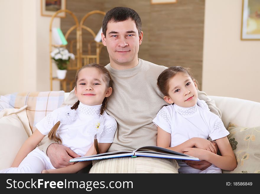 A father with her daughters at home in the living room reading a book. A father with her daughters at home in the living room reading a book