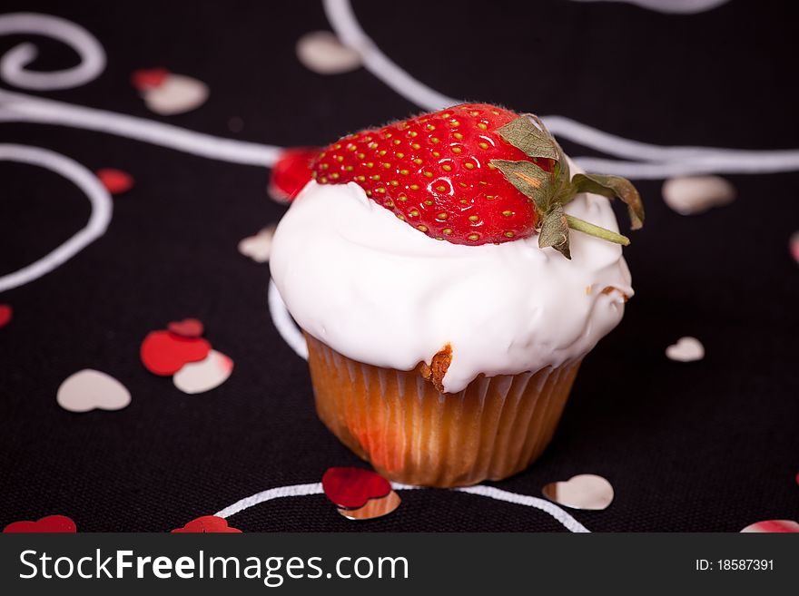 Cup cake with strawberry on black background with red hearts.