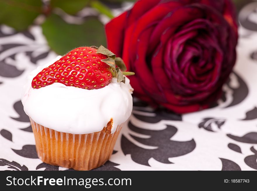 Cup cake decorated with strawberry on background with the rose.