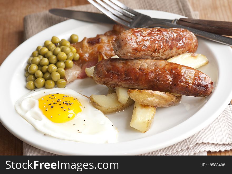 Freshly made English breakfast with sausages, chips, egg and peas on a plate