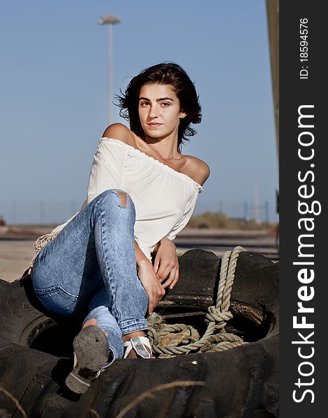 View of a beautiful young teenager sitting on top of an abandoned tractor wheel.