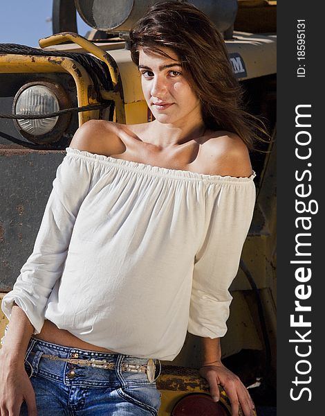 View of a beautiful girl on a fashion pose in front of a construction tractor.
