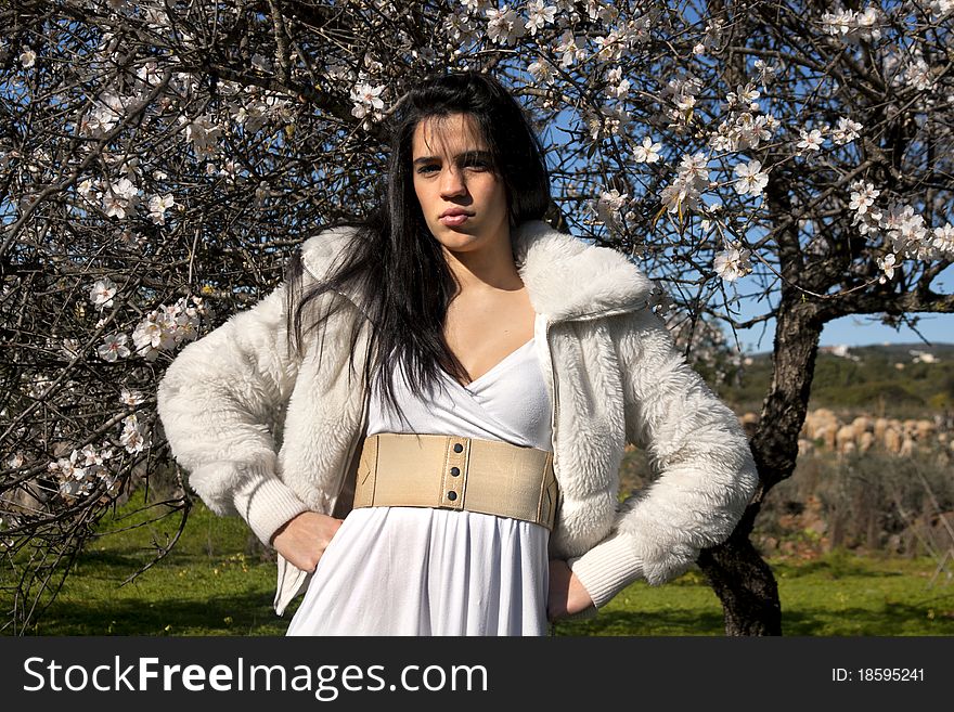 View of a beautiful girl on a white dress on a green grass field next to a almond tree. View of a beautiful girl on a white dress on a green grass field next to a almond tree