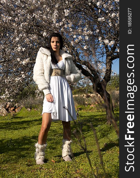 View of a beautiful girl on a white dress on a green grass field next to a almond tree. View of a beautiful girl on a white dress on a green grass field next to a almond tree