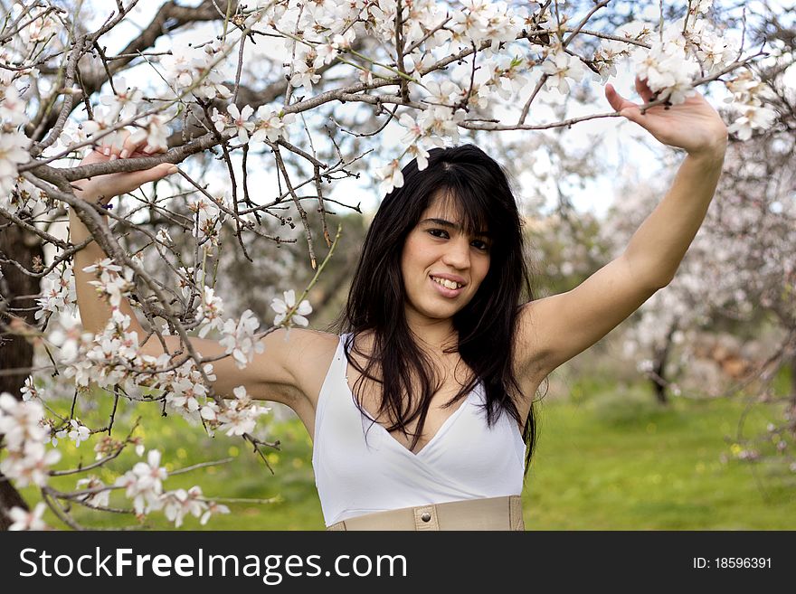 View of a beautiful girl on a white dress on a green grass field next to a almond tree. View of a beautiful girl on a white dress on a green grass field next to a almond tree