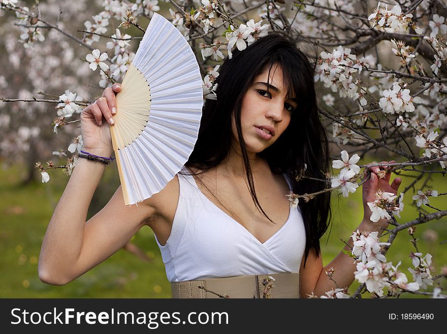 View of a beautiful girl on a white dress on a green grass field next to a almond tree. View of a beautiful girl on a white dress on a green grass field next to a almond tree