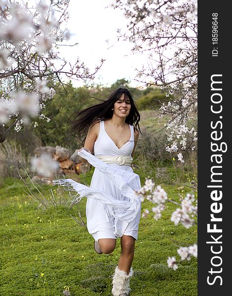 View of a beautiful girl on a white dress on a green grass field next to a almond tree. View of a beautiful girl on a white dress on a green grass field next to a almond tree