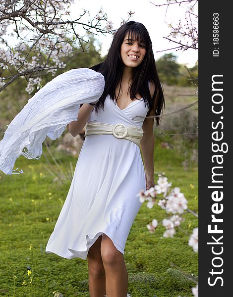 View of a beautiful girl on a white dress on a green grass field next to a almond tree. View of a beautiful girl on a white dress on a green grass field next to a almond tree