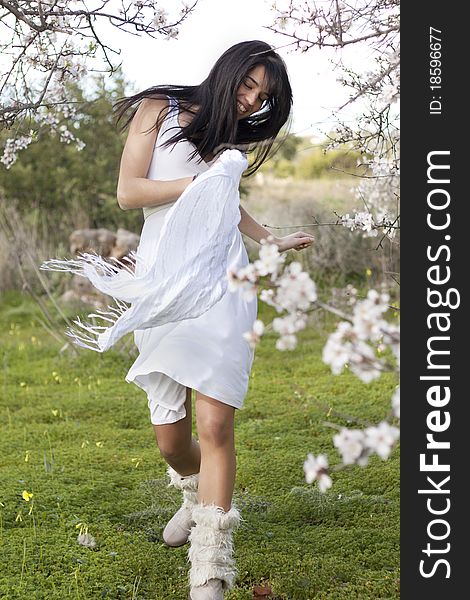 View of a beautiful girl on a white dress on a green grass field next to a almond tree. View of a beautiful girl on a white dress on a green grass field next to a almond tree