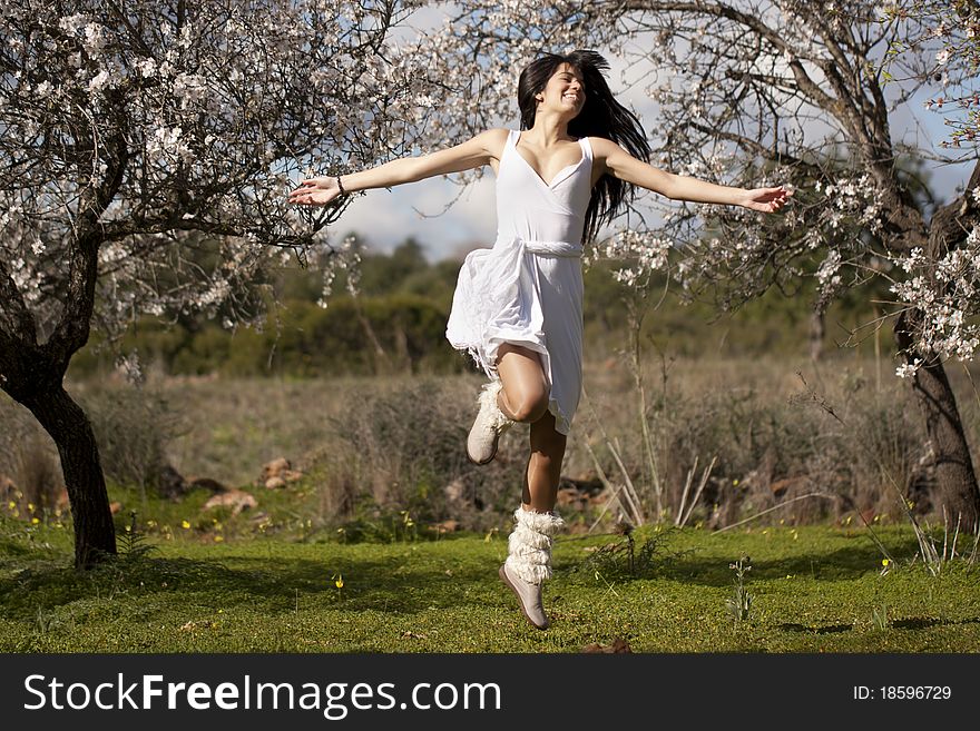 View of a beautiful girl on a white dress on a green grass field next to a almond tree. View of a beautiful girl on a white dress on a green grass field next to a almond tree