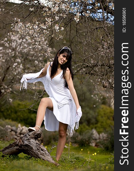 View of a beautiful girl on a white dress on a green grass field next to a almond tree. View of a beautiful girl on a white dress on a green grass field next to a almond tree