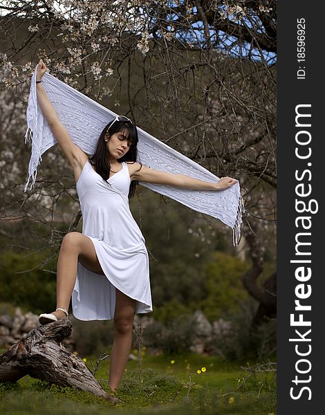 View of a beautiful girl on a white dress on a green grass field next to a almond tree. View of a beautiful girl on a white dress on a green grass field next to a almond tree