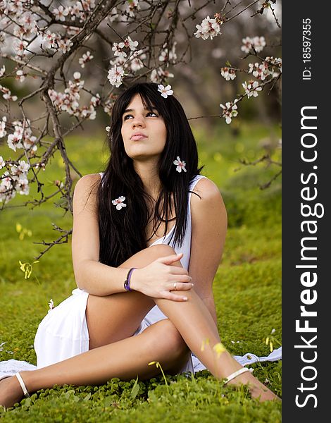 View of a beautiful girl on a white dress on a green grass field next to a almond tree. View of a beautiful girl on a white dress on a green grass field next to a almond tree