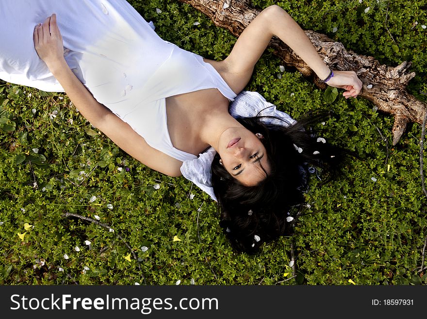 View of a beautiful girl on a white dress on a green grass field next to a almond tree. View of a beautiful girl on a white dress on a green grass field next to a almond tree