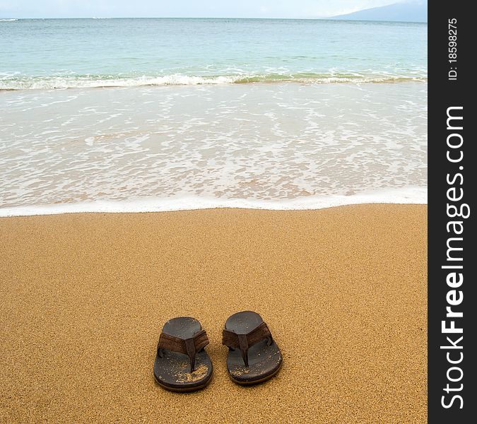 Beach sandals or tongs on a sandy beach with lots of background copyspace