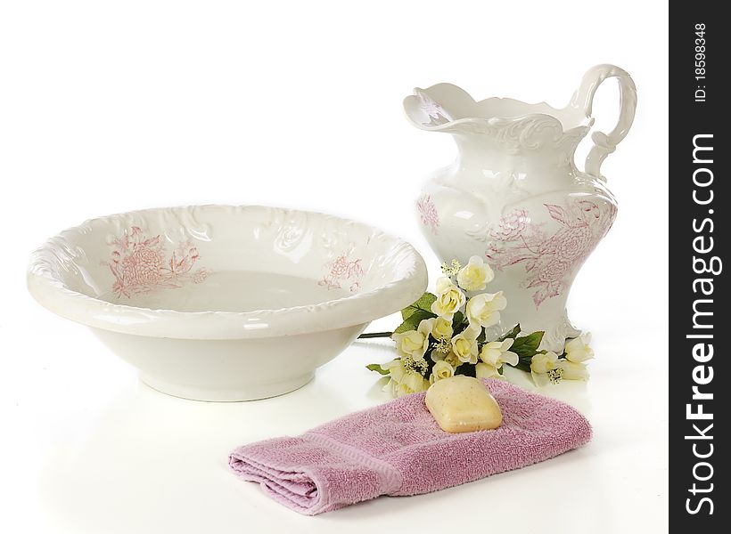 An antique bowl and pitcher with a bar of soap, hand towel and bouquet of soft yellow roses. Isolated on white. An antique bowl and pitcher with a bar of soap, hand towel and bouquet of soft yellow roses. Isolated on white.