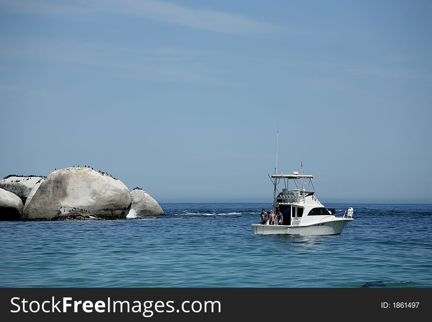 A boat on the ocean next to rock with penguins. A boat on the ocean next to rock with penguins