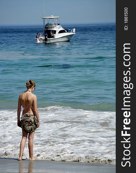 A woman standing in waves with boat in background. A woman standing in waves with boat in background