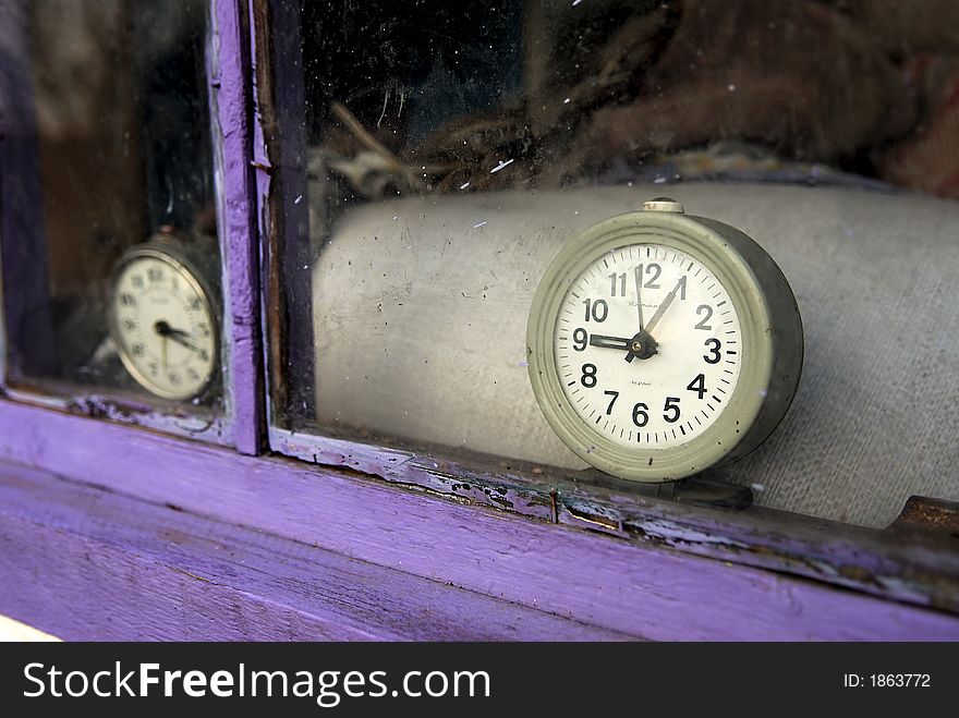 Old clocks are behind a window of a dilapidated house