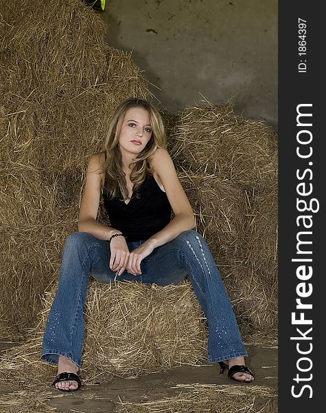 Beautiful blond teenager sitting on hay within a barn