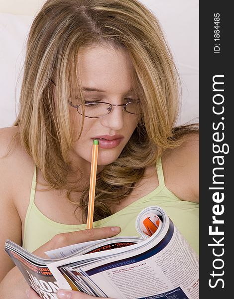 Beautiful blond teenager reading a book with glasses and holding pen. Beautiful blond teenager reading a book with glasses and holding pen