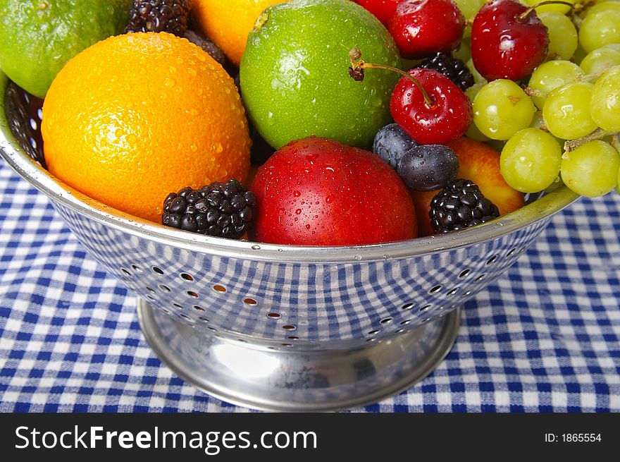 Freshly washed fruits drain in a stainless steel colander.