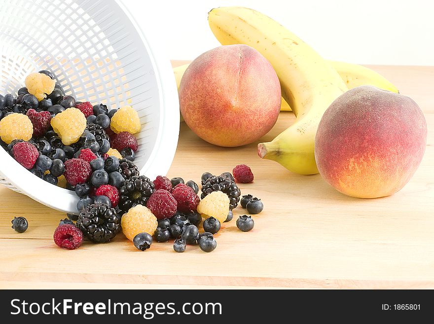 A cutting board full of fruit waiting to become a salad or desert, it consists of peaches, bananas,blueberries,blackberries,red raspberries and golden raspberries. A cutting board full of fruit waiting to become a salad or desert, it consists of peaches, bananas,blueberries,blackberries,red raspberries and golden raspberries.