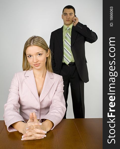 Woman's sitting at the office desk. Man's standing behind her and talking mobile phone. Woman's sitting at the office desk. Man's standing behind her and talking mobile phone.