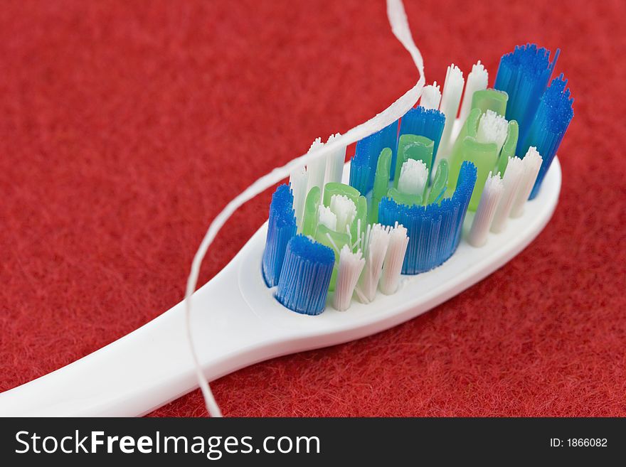 White toothbrush with blue and green bristles and dental floss on red background. White toothbrush with blue and green bristles and dental floss on red background