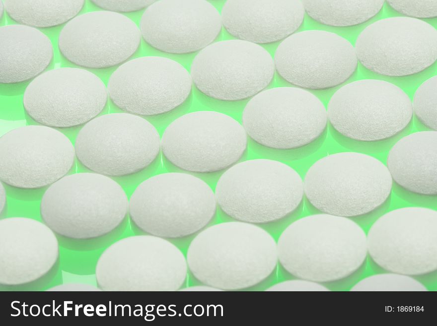 Round white pills sit on a bright green table. Round white pills sit on a bright green table.