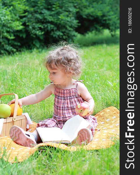 Small lovely girl with fruits and book in the park. Small lovely girl with fruits and book in the park