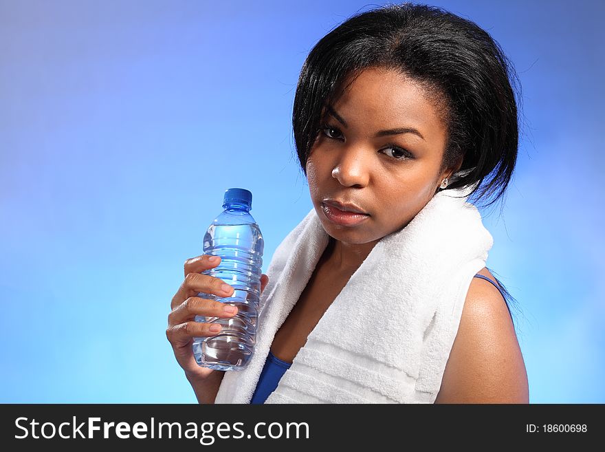 Landscape close up of beautiful black woman, looking tired after working out. She is wearing a blue vest, has a white towel around her shoulders and holding a bottle of water. Landscape close up of beautiful black woman, looking tired after working out. She is wearing a blue vest, has a white towel around her shoulders and holding a bottle of water.